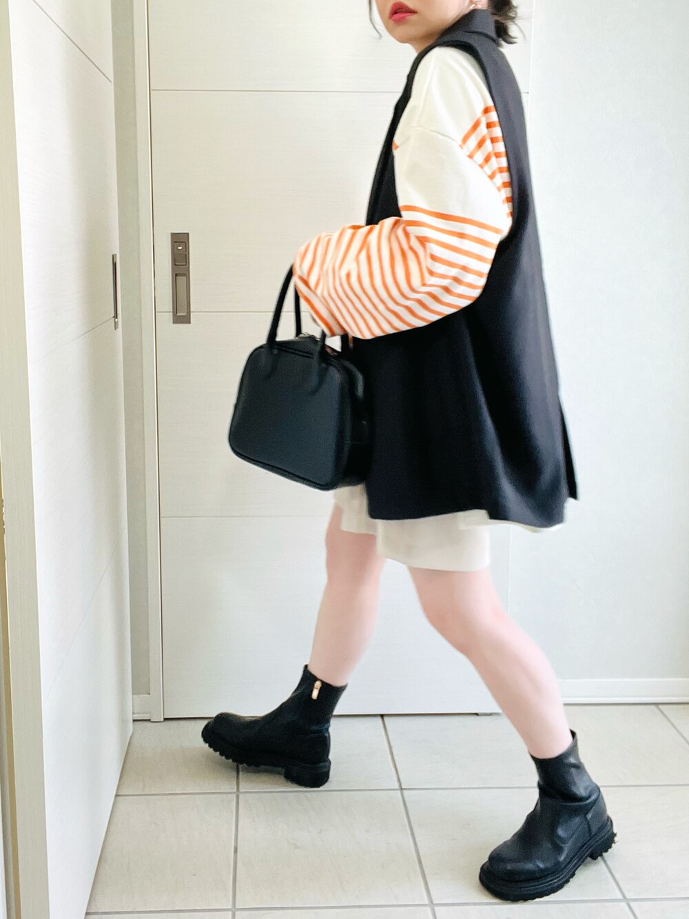 オレンジ系のTシャツ/カットソー、ブラック系のベスト、ホワイト系のスラックスを着用したレディースの春コーディネートの3枚目の写真