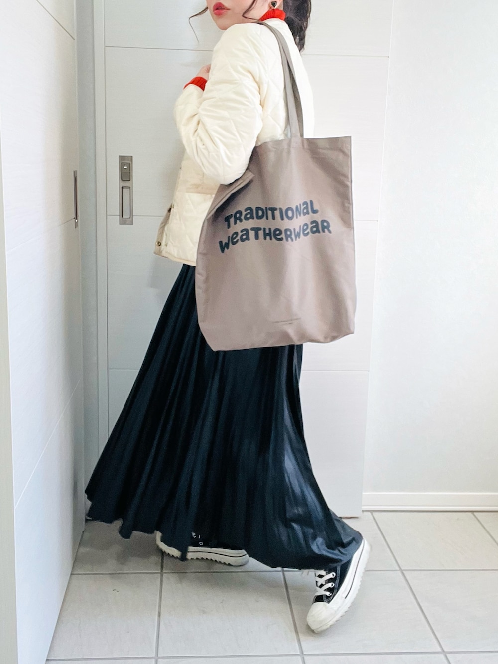 ホワイト系のノーカラージャケット、オレンジ系のニット/セーター、ブラック系のスカートを着用したレディースの秋コーディネートの4枚目の写真