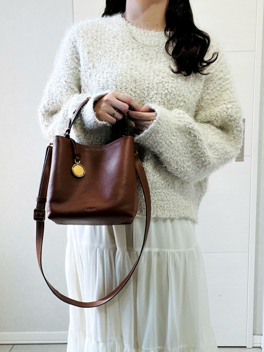 ブラウン系のショルダーバッグ、ベージュ系のニット/セーター、ホワイト系のスカートを着用したレディースの秋コーディネートの2枚目の写真