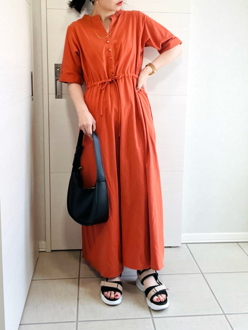 オレンジ系のワンピース、ベージュ系のサンダル、ブラック系のショルダーバッグを着用したレディースの夏コーディネートの2枚目の写真