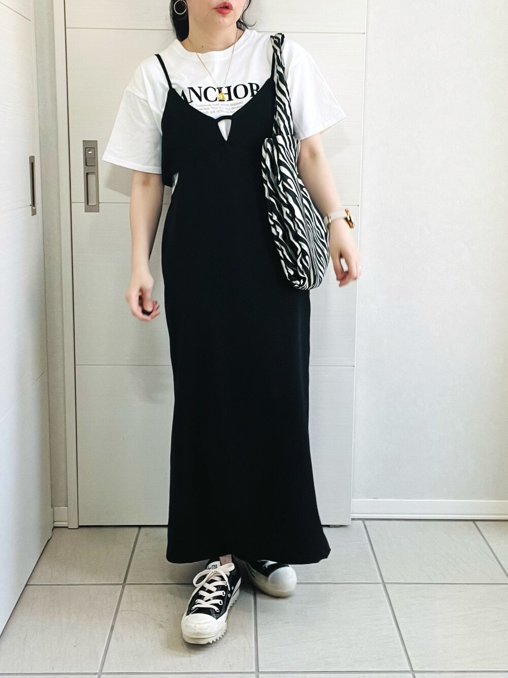 ホワイト系のTシャツ/カットソー、ブラック系のジャンパースカート、ブラック系のスニーカーを着用したレディースの春コーディネートの2枚目の写真