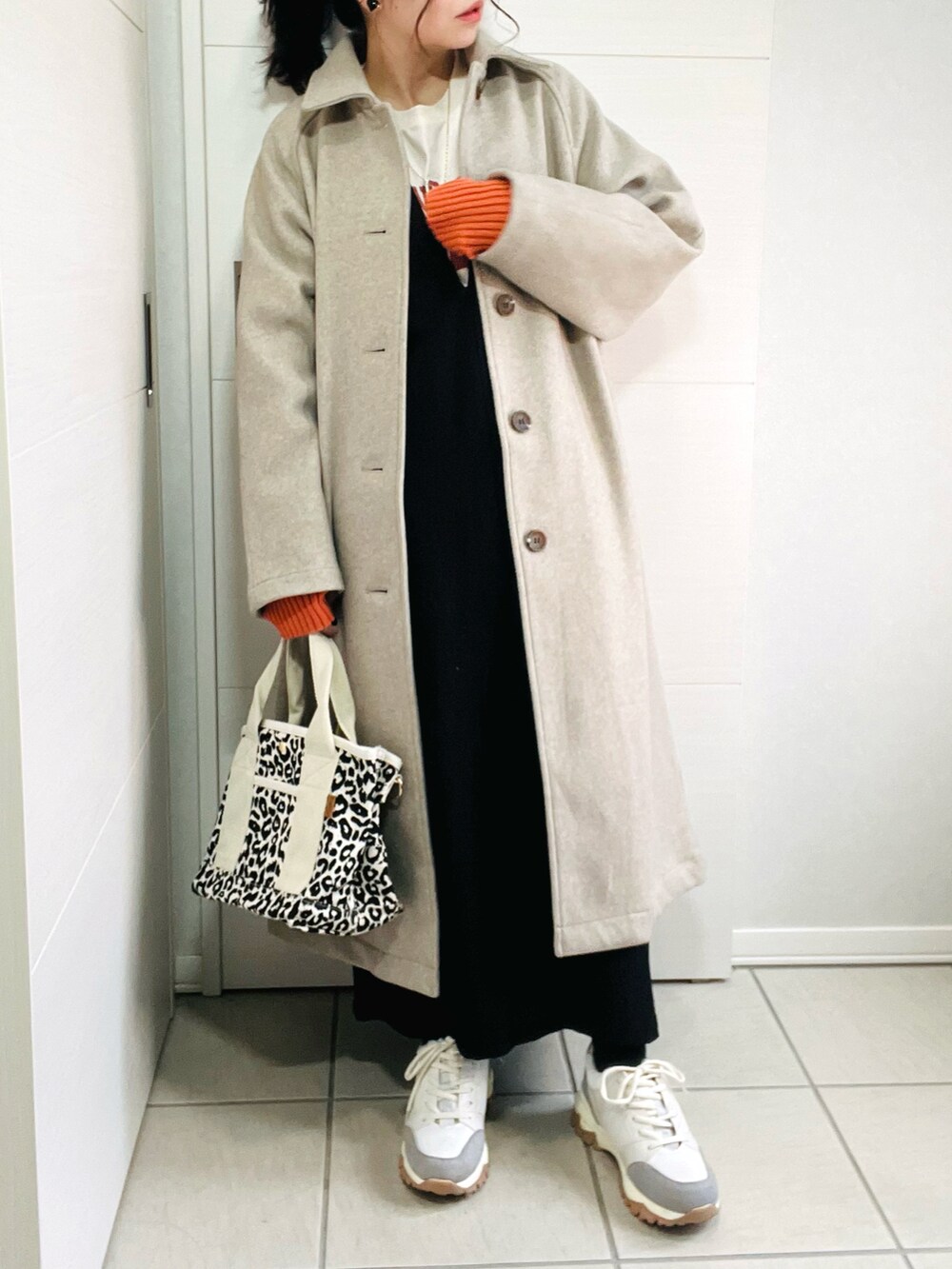 ベージュ系のステンカラーコート、ベージュ系のTシャツ/カットソー、ブラック系のワンピースを着用したレディースの秋コーディネートの3枚目の写真