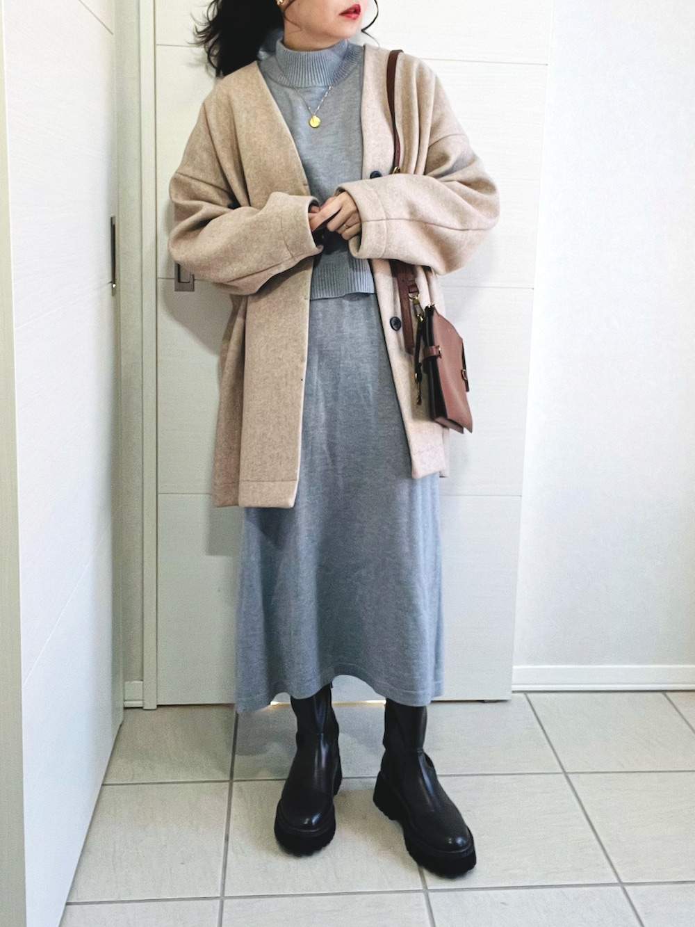 グレー系のワンピース、ピンク系のノーカラーコート、ブラウン系のブーツを着用したレディースの冬コーディネートの2枚目の写真