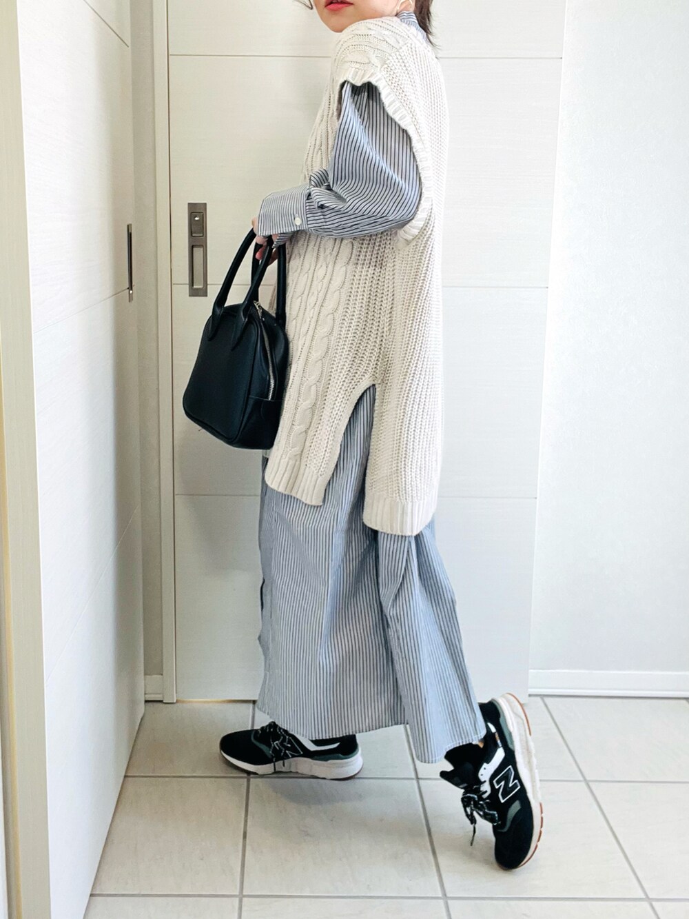 ブラック系のワンピース、ホワイト系のベスト、ブラック系のスニーカーを着用したレディースの春コーディネートの3枚目の写真