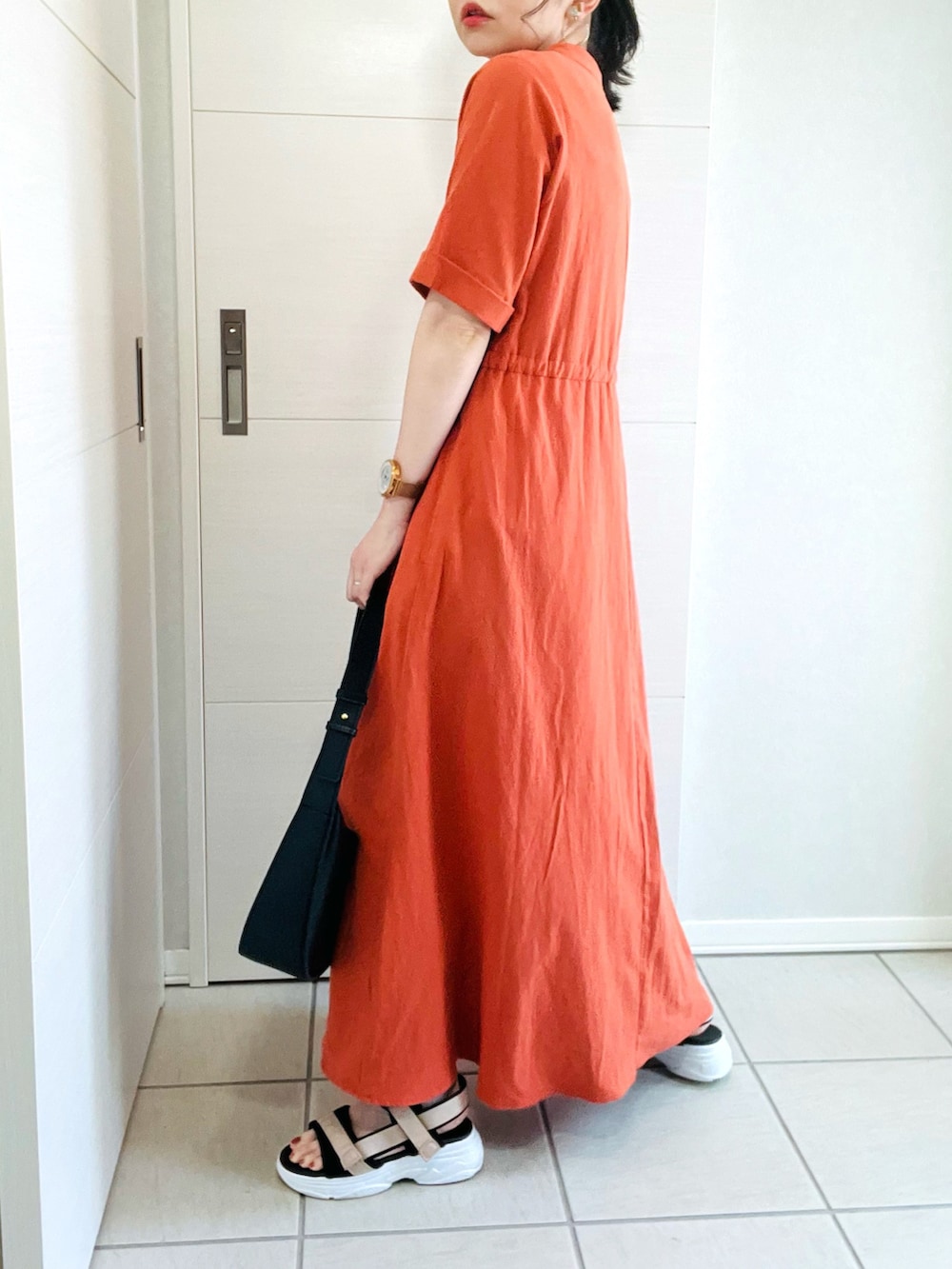 オレンジ系のワンピース、ベージュ系のサンダル、ブラック系のショルダーバッグを着用したレディースの夏コーディネートの4枚目の写真