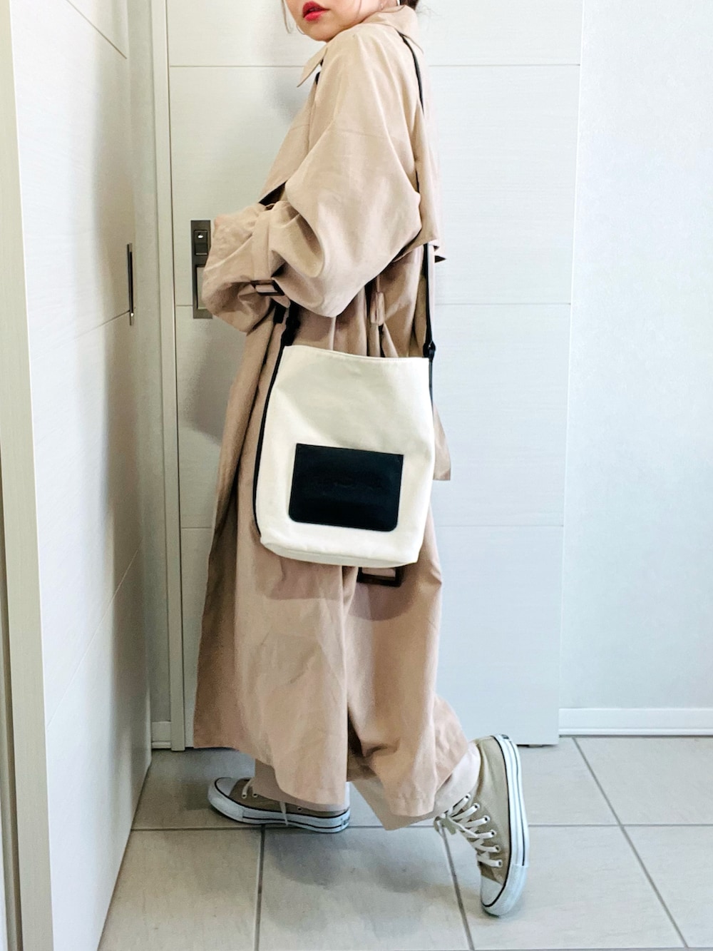 ベージュ系のトレンチコート、ブラウン系のTシャツ/カットソー、ホワイト系のスラックスを着用したレディースの冬コーディネートの4枚目の写真