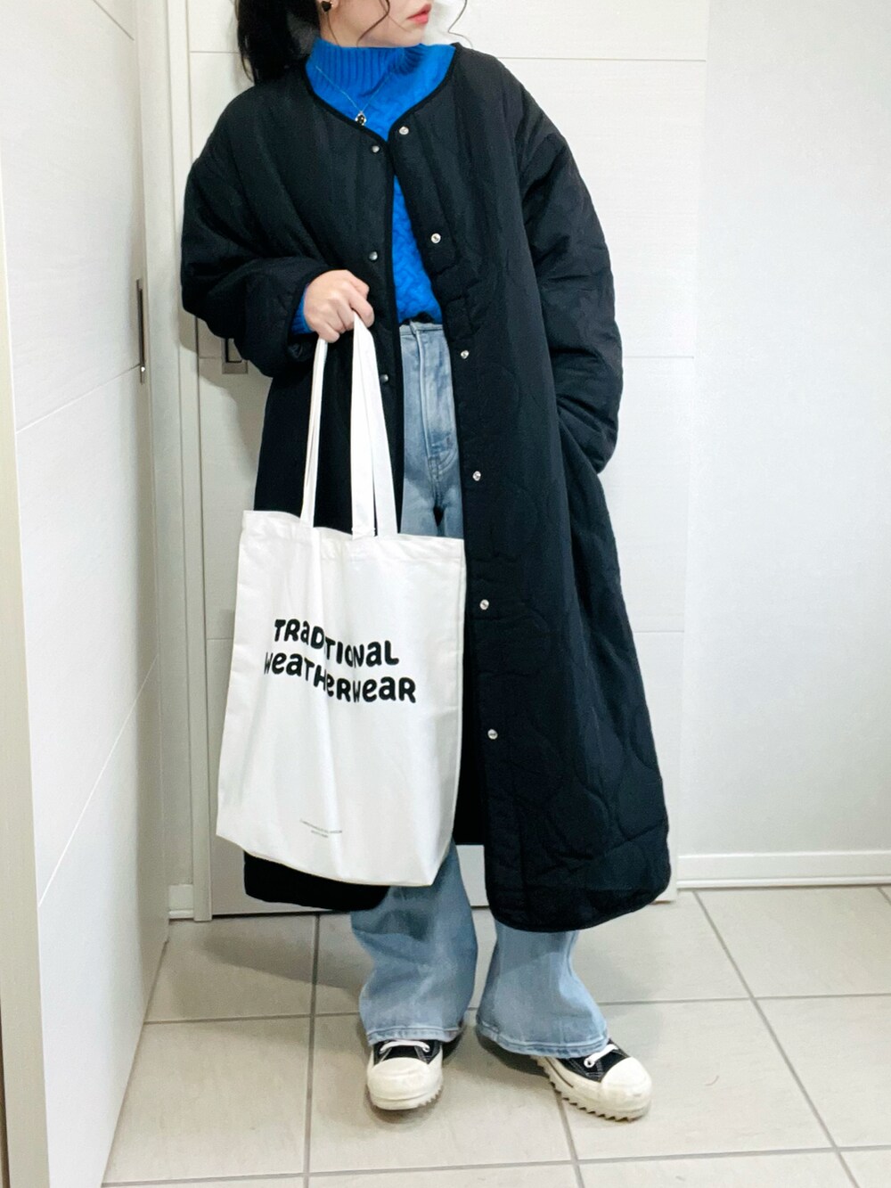 ブラック系のノーカラーコート、ブルー系のニット/セーター、ブルー系のデニムパンツを着用したレディースの秋コーディネートの3枚目の写真