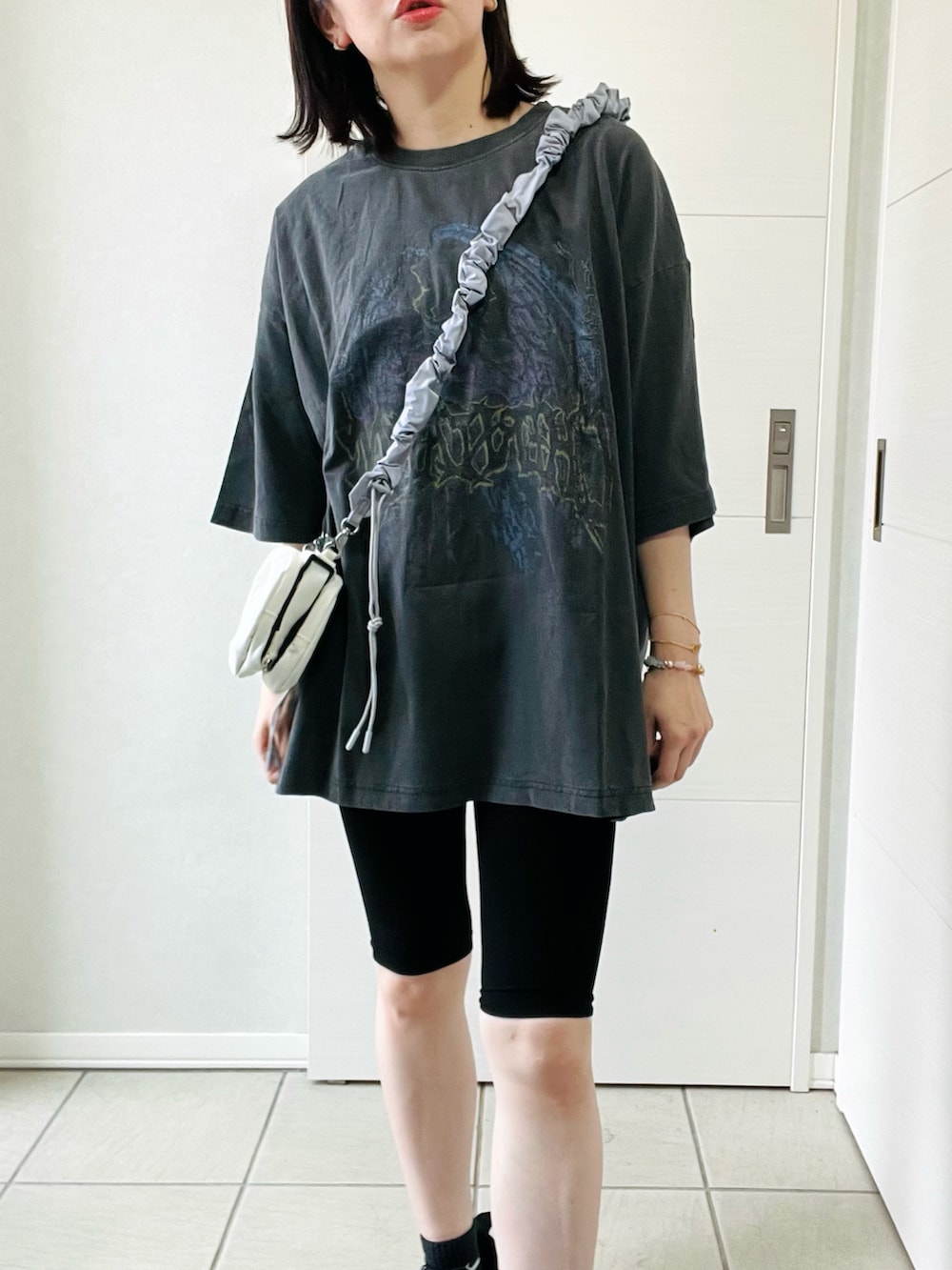 グレー系のTシャツ/カットソー、ブラック系のスニーカー、ホワイト系のショルダーバッグを着用したレディースの夏コーディネートの2枚目の写真