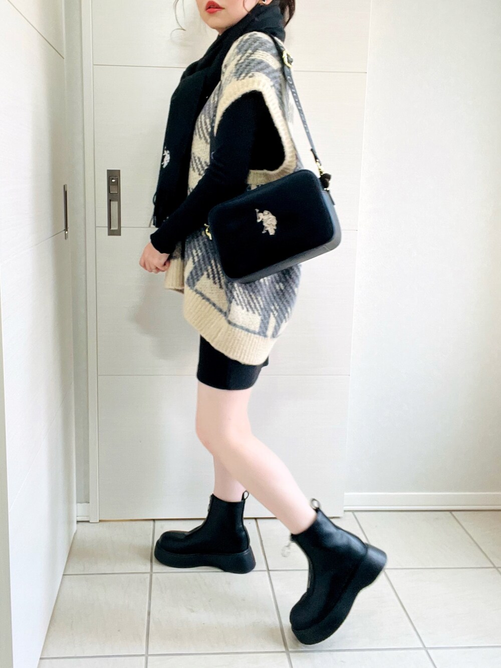 ブラック系のスカート、ホワイト系のベスト、ブラック系のブーツを着用したレディースの秋コーディネートの4枚目の写真