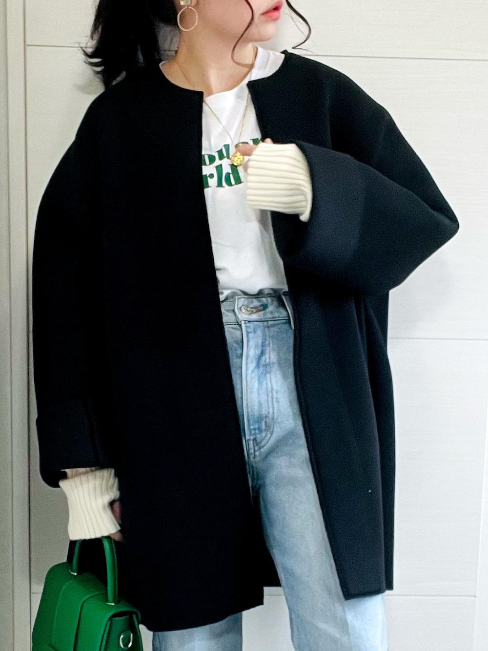 ブラック系のノーカラーコート、ホワイト系のTシャツ/カットソー、ブルー系のデニムパンツを着用したレディースの秋コーディネートの3枚目の写真