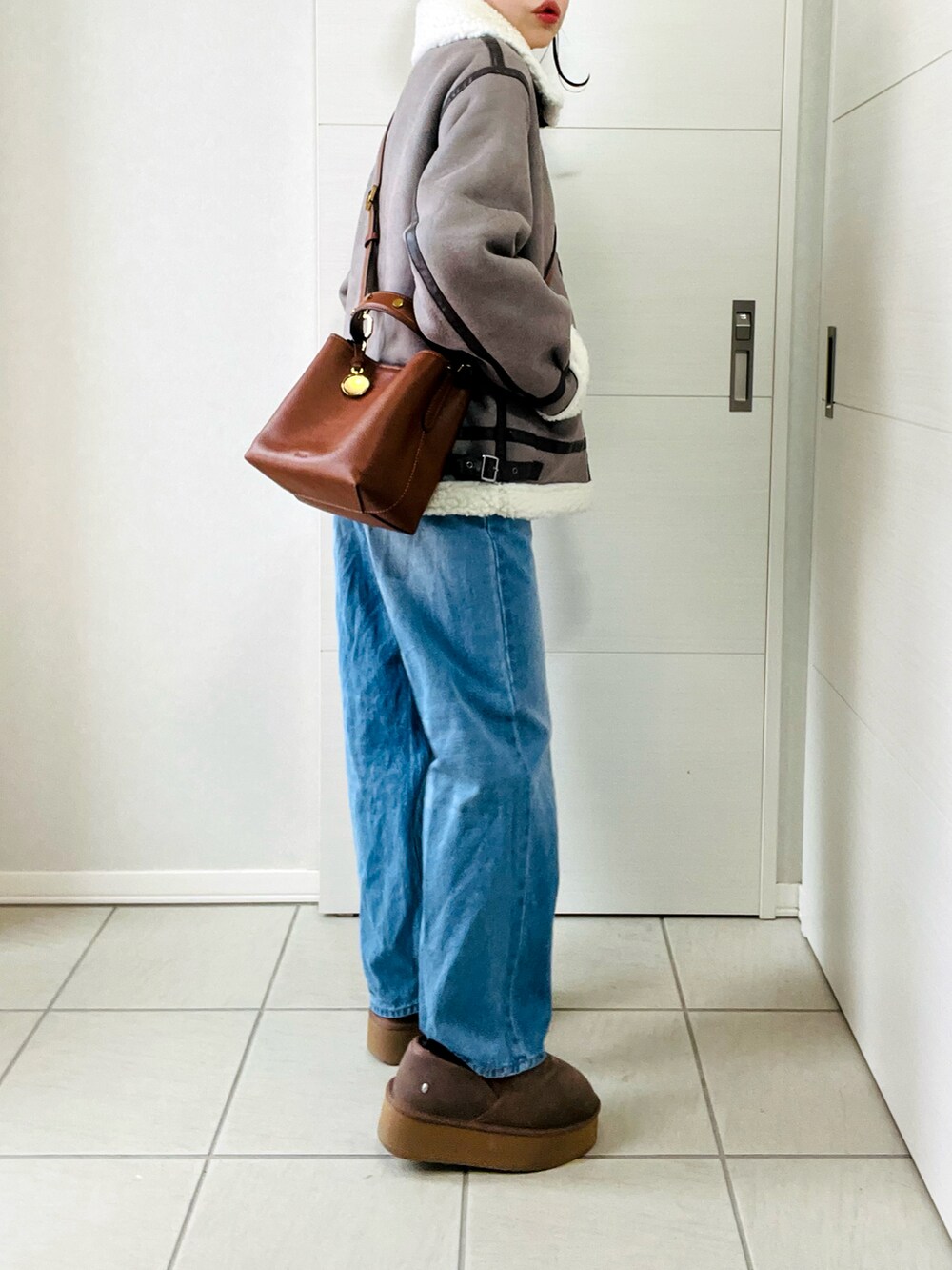 グレー系のムートンコート、ブルー系のデニムパンツ、ベージュ系のスリッポンを着用したレディースの冬コーディネートの5枚目の写真