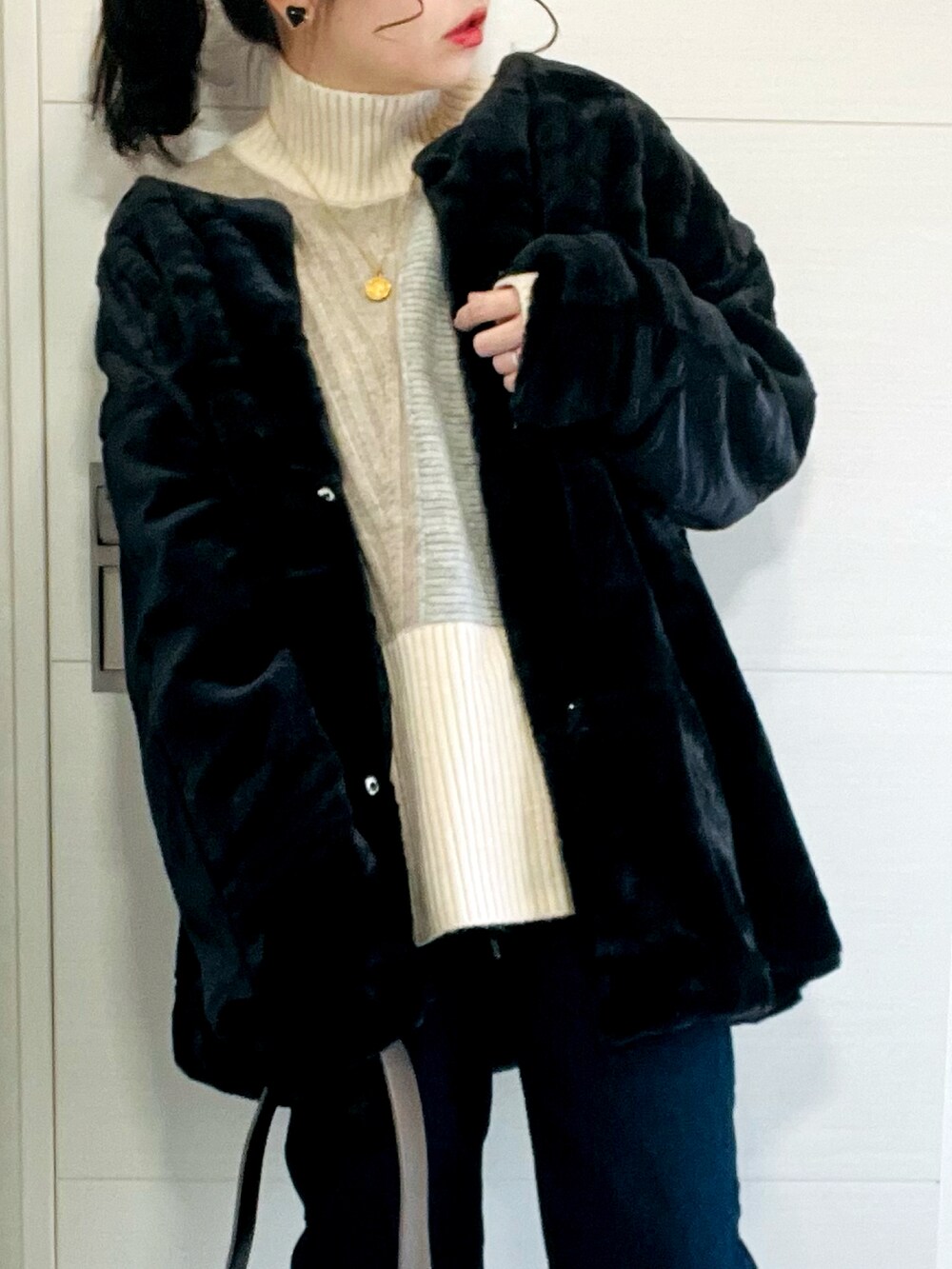 ブラック系のノーカラーコート、ベージュ系のニット/セーター、ブルー系のデニムパンツを着用したレディースの冬コーディネートの2枚目の写真