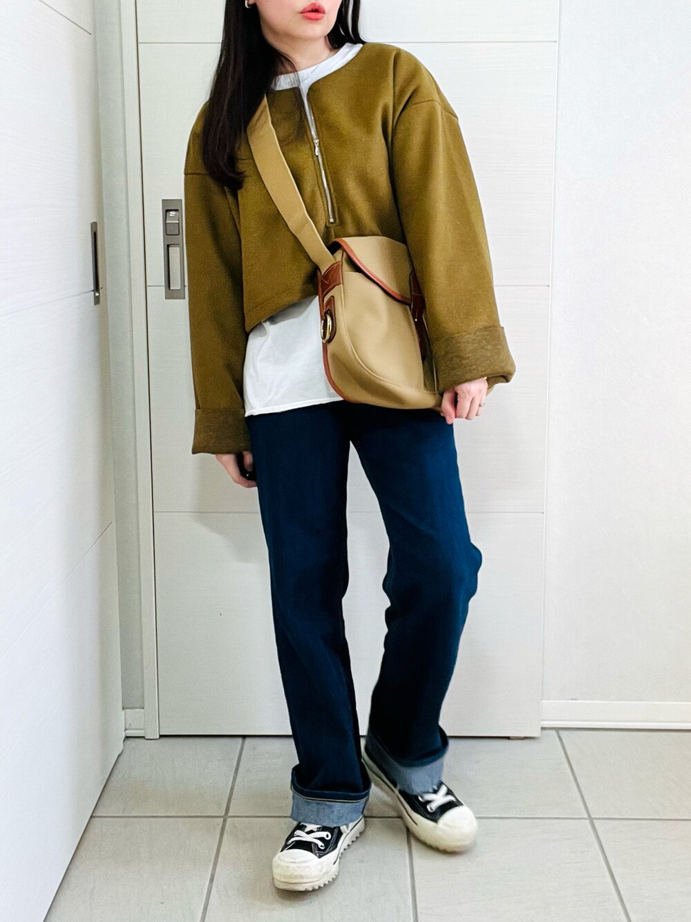 グリーン系のワンピース、ブルー系のデニムパンツ、ブラック系のスニーカーを着用したレディースの冬コーディネートの2枚目の写真