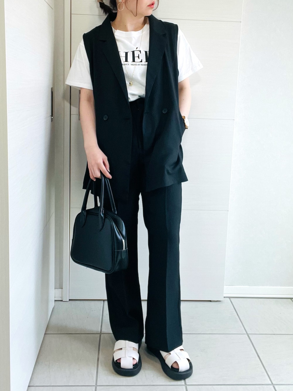 ブラック系のベスト、ホワイト系のTシャツ/カットソー、ブラック系のスラックスを着用したレディースの春コーディネートの2枚目の写真