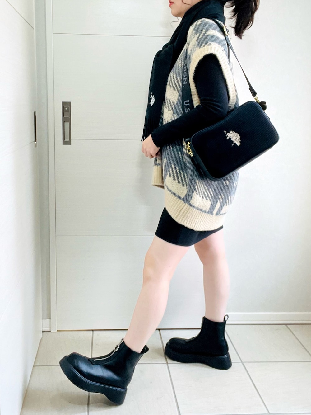 ブラック系のスカート、ホワイト系のベスト、ブラック系のブーツを着用したレディースの秋コーディネートの3枚目の写真