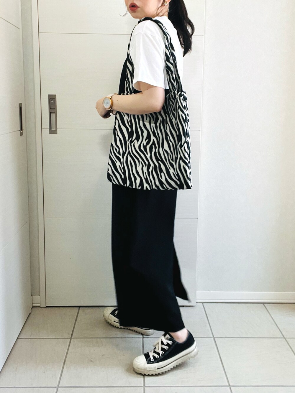 ホワイト系のTシャツ/カットソー、ブラック系のジャンパースカート、ブラック系のスニーカーを着用したレディースの春コーディネートの4枚目の写真