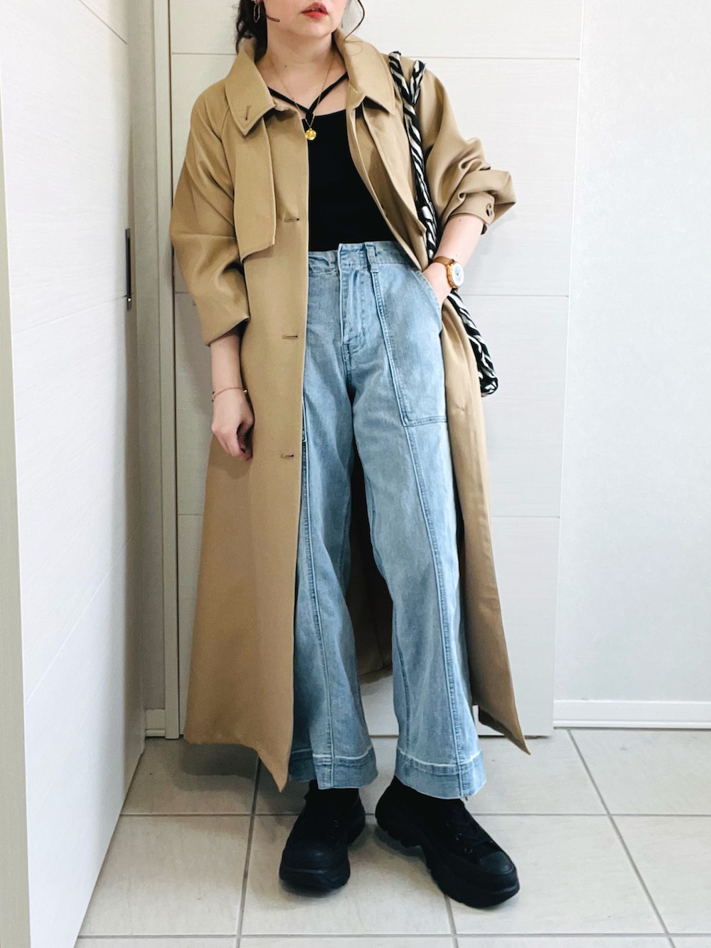 ベージュ系のトレンチコート、ブラック系のキャミソール、ブルー系のデニムパンツを着用したレディースの春コーディネートの2枚目の写真