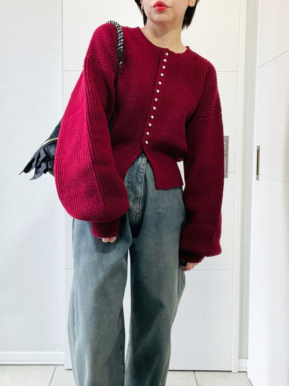 レッド系のカーディガン/ボレロ、ブラック系のブーツ、ブルー系のデニムパンツを着用したレディースの秋コーディネートの2枚目の写真