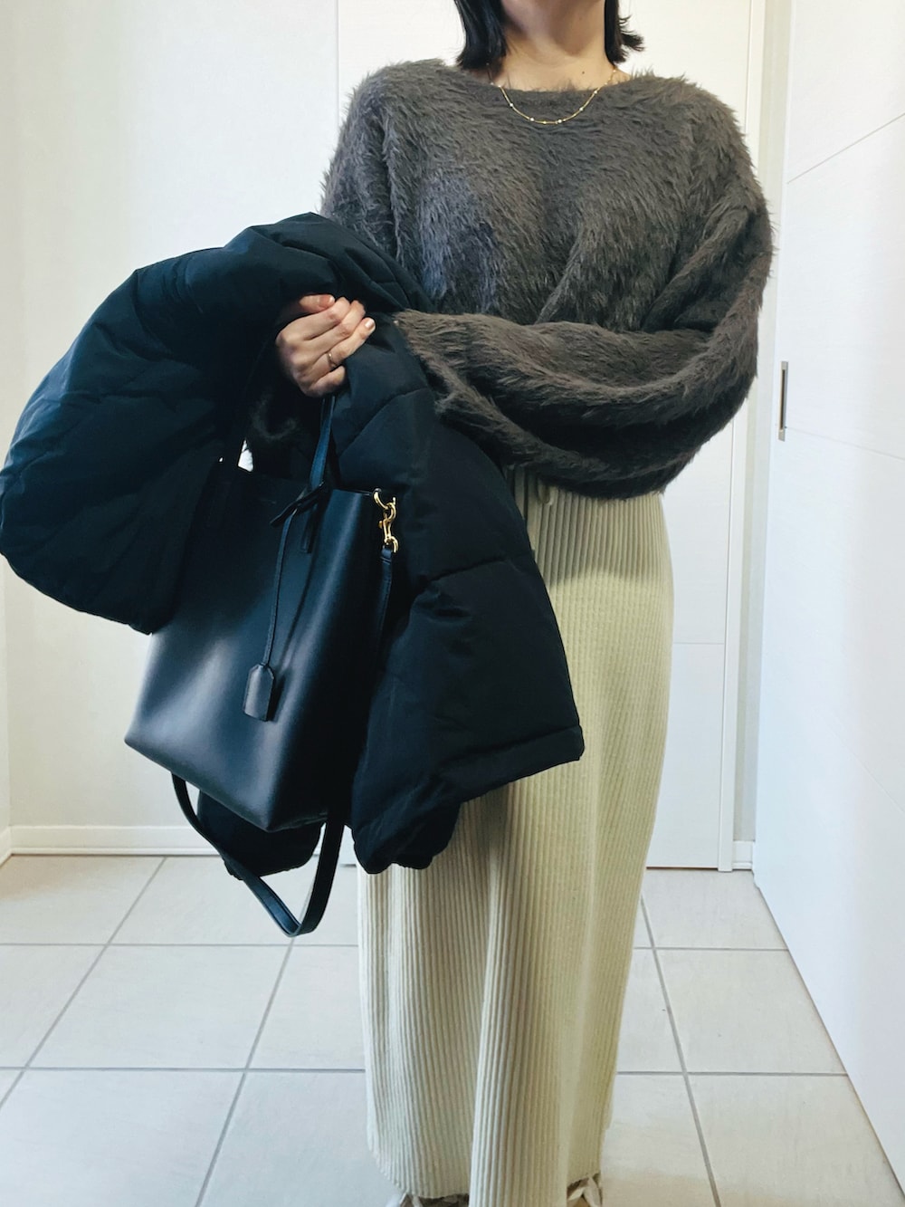 ブラック系のダウンジャケット/コート、グレー系のニット/セーター、ホワイト系のスカートを着用したレディースの冬コーディネートの5枚目の写真