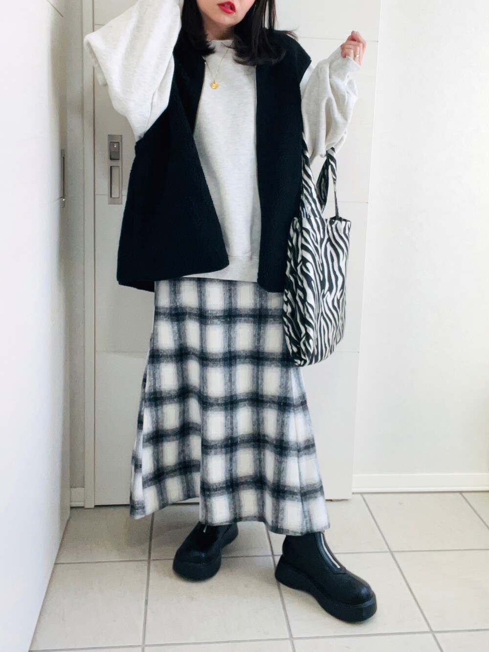 ブラック系のベスト、グレー系のスウェット、ホワイト系のスカートを着用したレディースの冬コーディネートの2枚目の写真