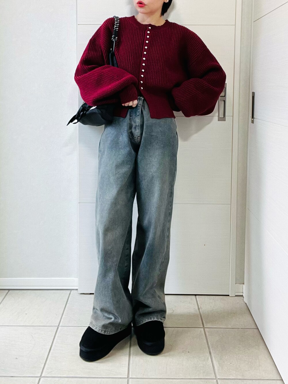 レッド系のカーディガン/ボレロ、ブラック系のブーツ、ブルー系のデニムパンツを着用したレディースの秋コーディネートの4枚目の写真