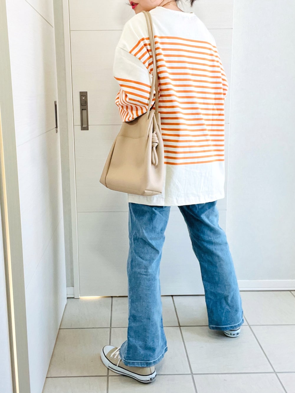 オレンジ系のTシャツ/カットソー、ブルー系のデニムパンツ、ベージュ系のトートバッグを着用したレディースの冬コーディネートの3枚目の写真