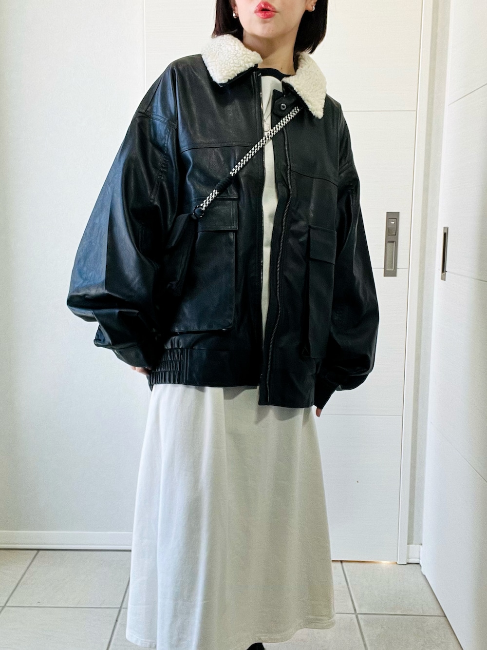 ブラック系のブルゾン、ホワイト系のワンピース、ブラック系のブーツを着用したレディースの冬コーディネートの2枚目の写真