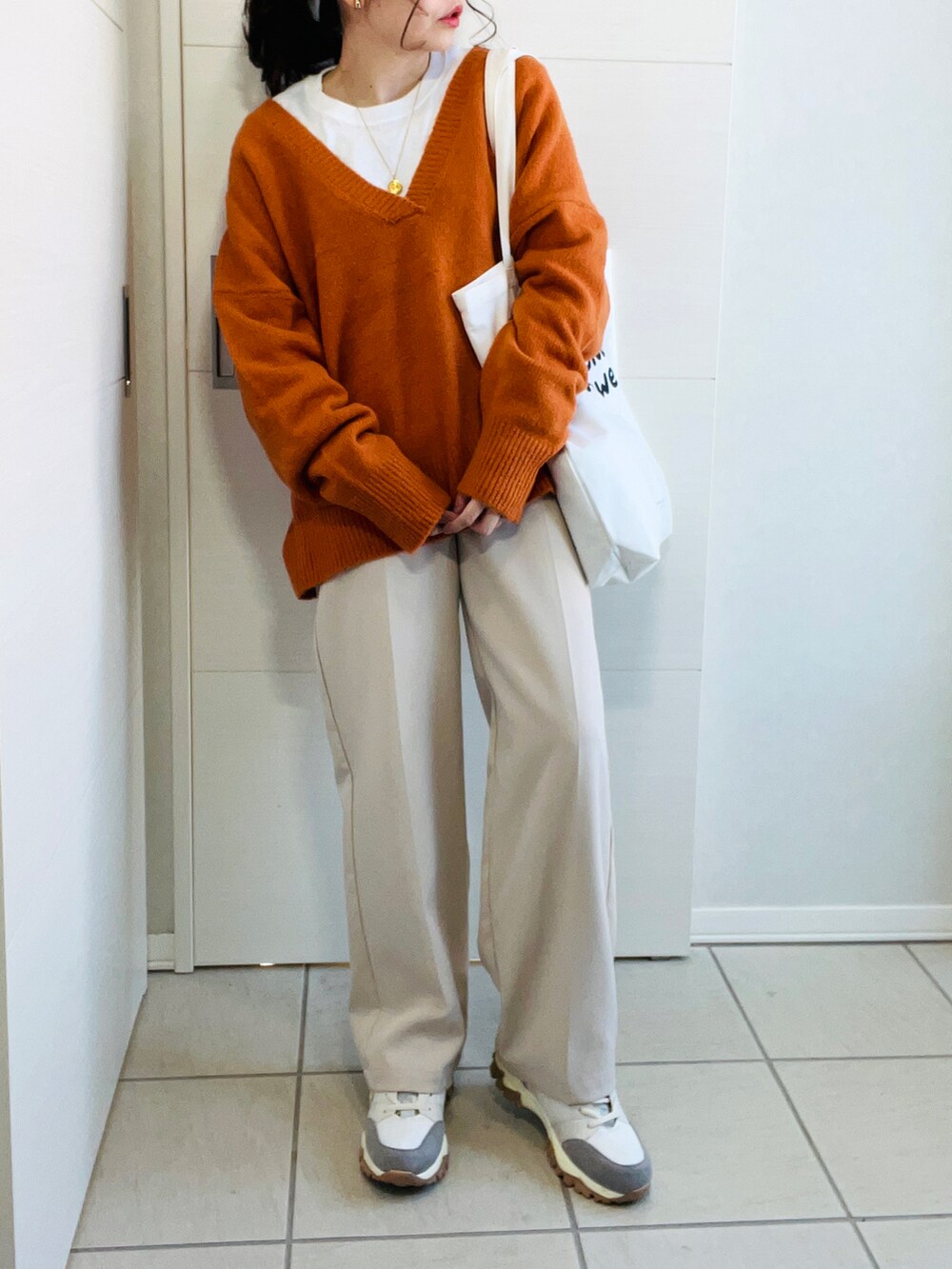 オレンジ系のニット/セーター、ホワイト系のスラックス、ベージュ系のスニーカーを着用したレディースの冬コーディネートの2枚目の写真