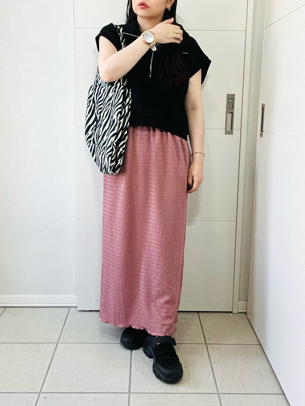 ブラック系のベスト、ピンク系のスカート、ブラック系のサンダルを着用したレディースの夏コーディネートの3枚目の写真