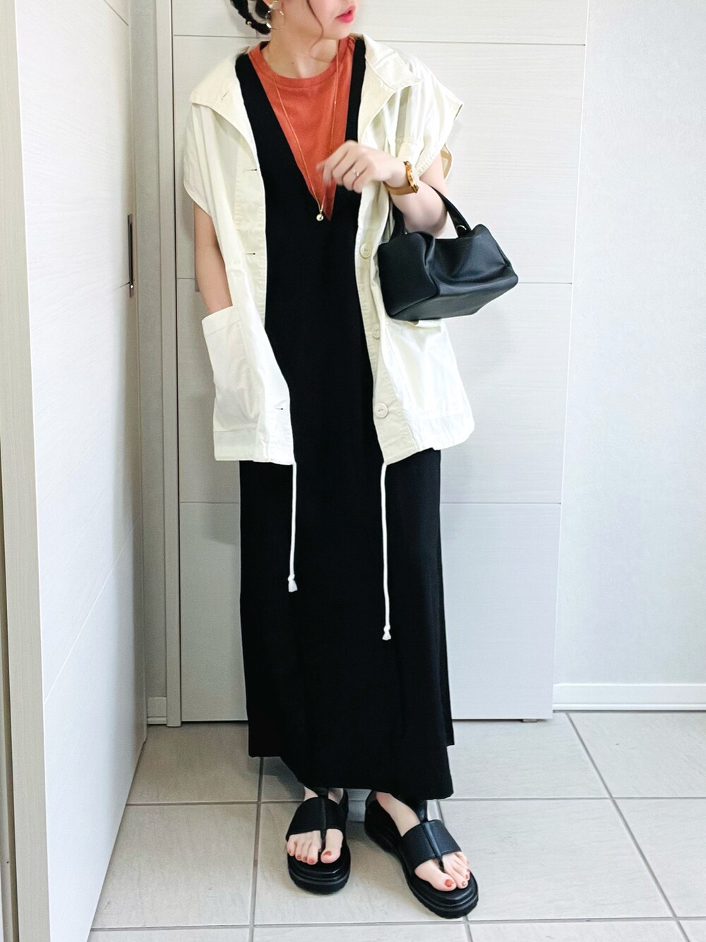 ホワイト系のベスト、オレンジ系のTシャツ/カットソー、ブラック系のワンピースを着用したレディースの夏コーディネートの2枚目の写真