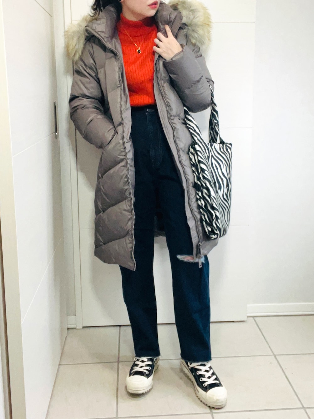 ブラウン系のダウンジャケット/コート、オレンジ系のニット/セーター、ブルー系のデニムパンツを着用したレディースの秋コーディネートの3枚目の写真