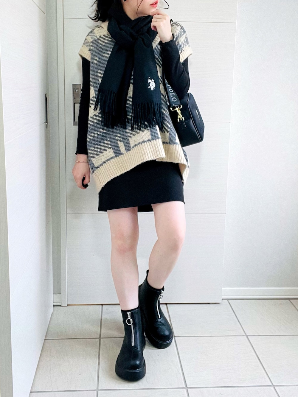 ブラック系のスカート、ホワイト系のベスト、ブラック系のブーツを着用したレディースの秋コーディネートの2枚目の写真