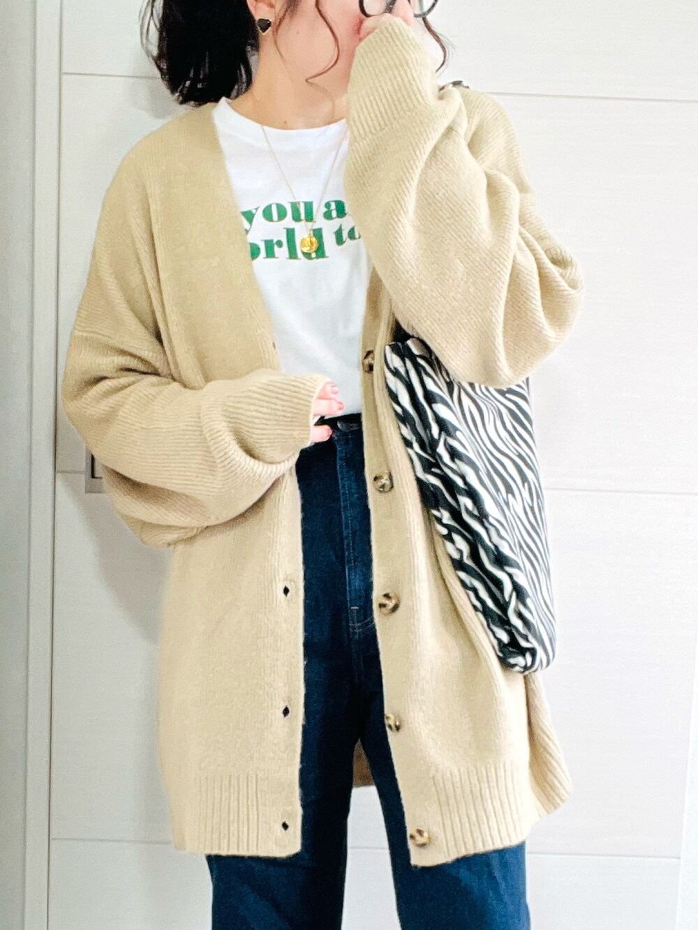 ベージュ系のカーディガン/ボレロ、ホワイト系のTシャツ/カットソー、ブルー系のデニムパンツを着用したレディースの秋コーディネートの3枚目の写真