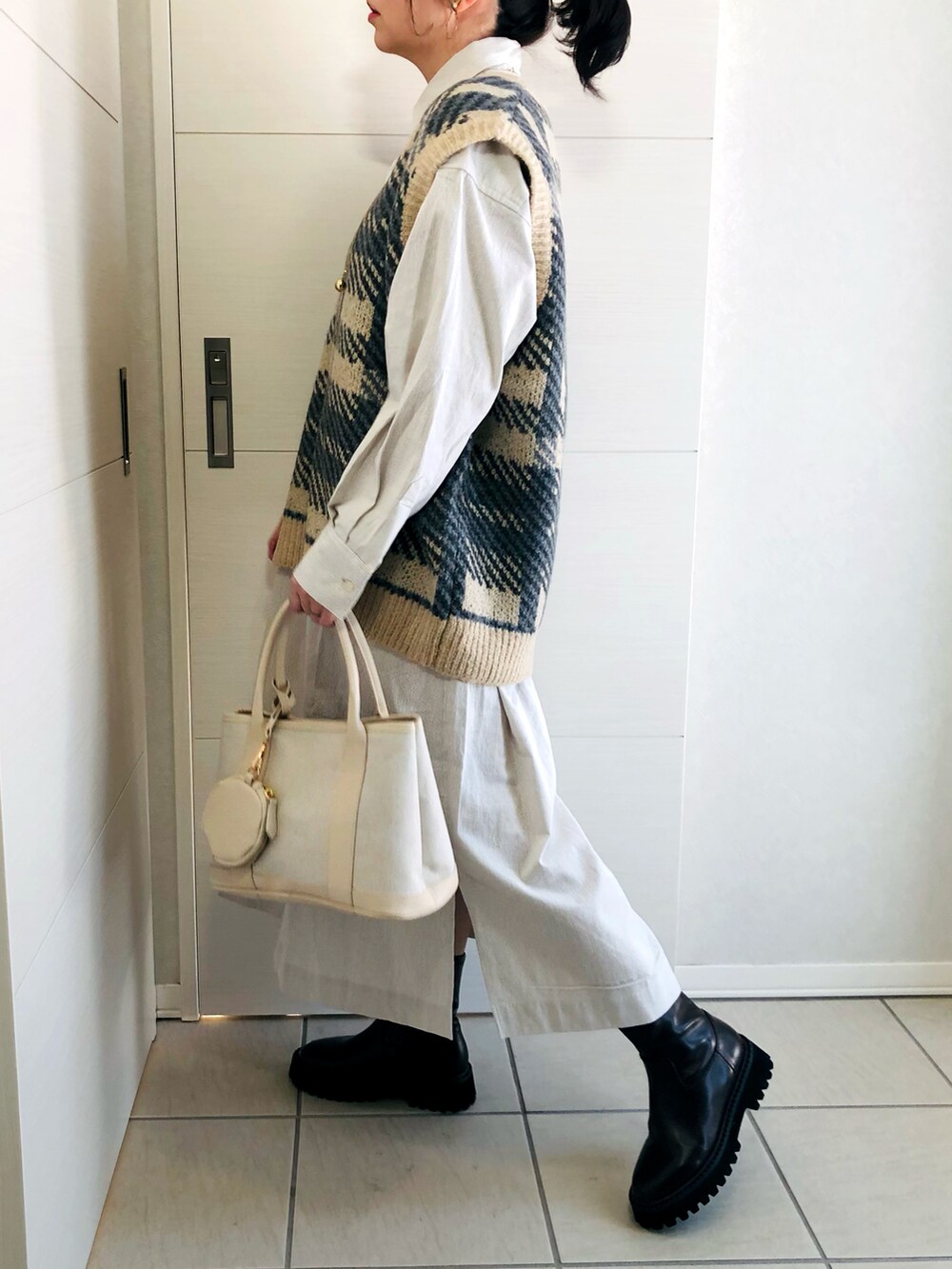 ベージュ系のワンピース、ホワイト系のベスト、ブラウン系のブーツを着用したレディースの冬コーディネートの4枚目の写真