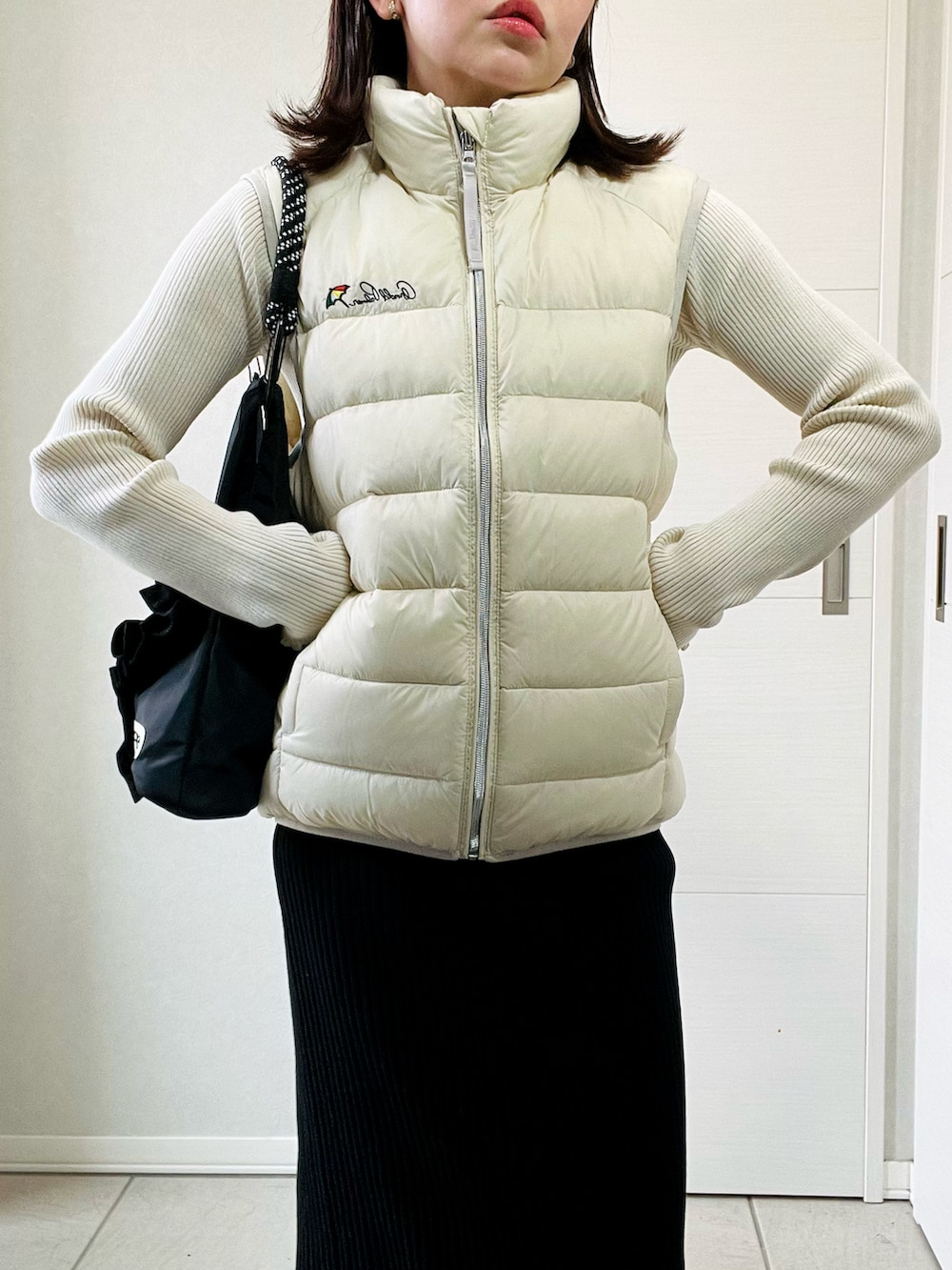 ホワイト系のダウンベスト、ホワイト系のニット/セーター、ブラック系のスカートを着用したレディースの秋コーディネートの2枚目の写真