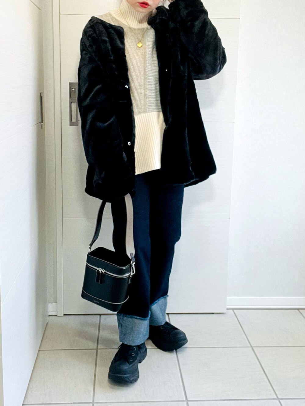 ブラック系のノーカラーコート、ベージュ系のニット/セーター、ブルー系のデニムパンツを着用したレディースの冬コーディネートの3枚目の写真