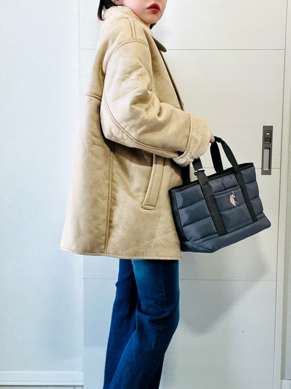 ベージュ系のムートンコート、ブルー系のデニムパンツ、グレー系のトートバッグを着用したレディースの冬コーディネートの3枚目の写真