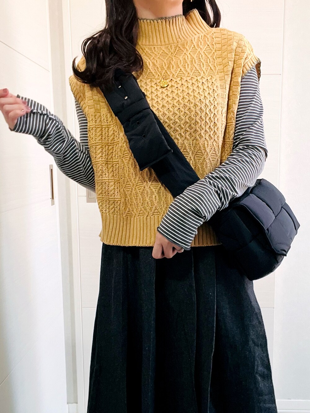 イエロー系のベスト、グレー系のTシャツ/カットソー、ブラック系のスカートを着用したレディースの秋コーディネートの3枚目の写真