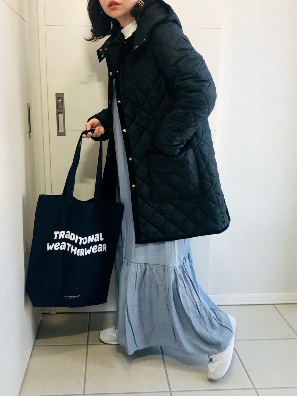 ブラック系のノーカラーコート、ブルー系のワンピース、ホワイト系のスニーカーを着用したレディースの冬コーディネートの2枚目の写真