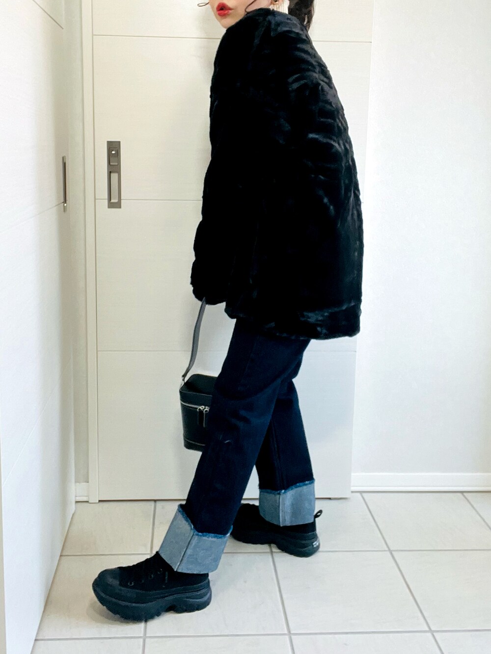 ブラック系のノーカラーコート、ベージュ系のニット/セーター、ブルー系のデニムパンツを着用したレディースの冬コーディネートの4枚目の写真