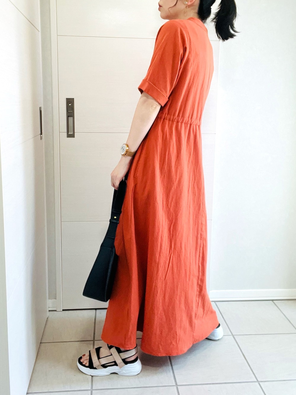 オレンジ系のワンピース、ベージュ系のサンダル、ブラック系のショルダーバッグを着用したレディースの夏コーディネートの5枚目の写真