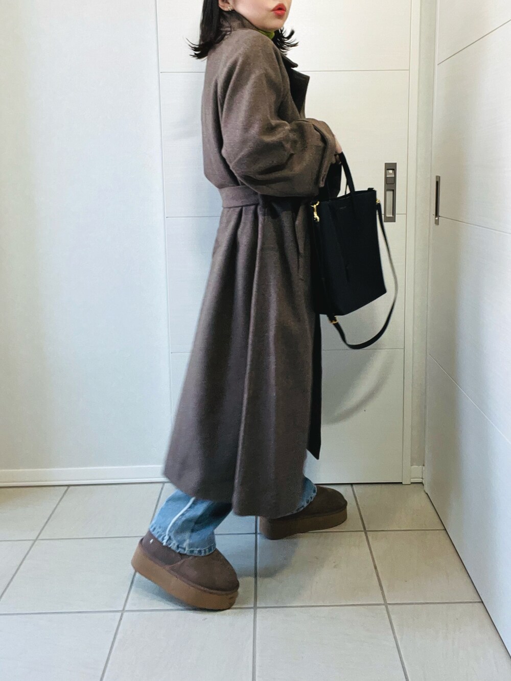 ブラウン系のステンカラーコート、グリーン系のニット/セーター、ブルー系のデニムパンツを着用したレディースの冬コーディネートの5枚目の写真