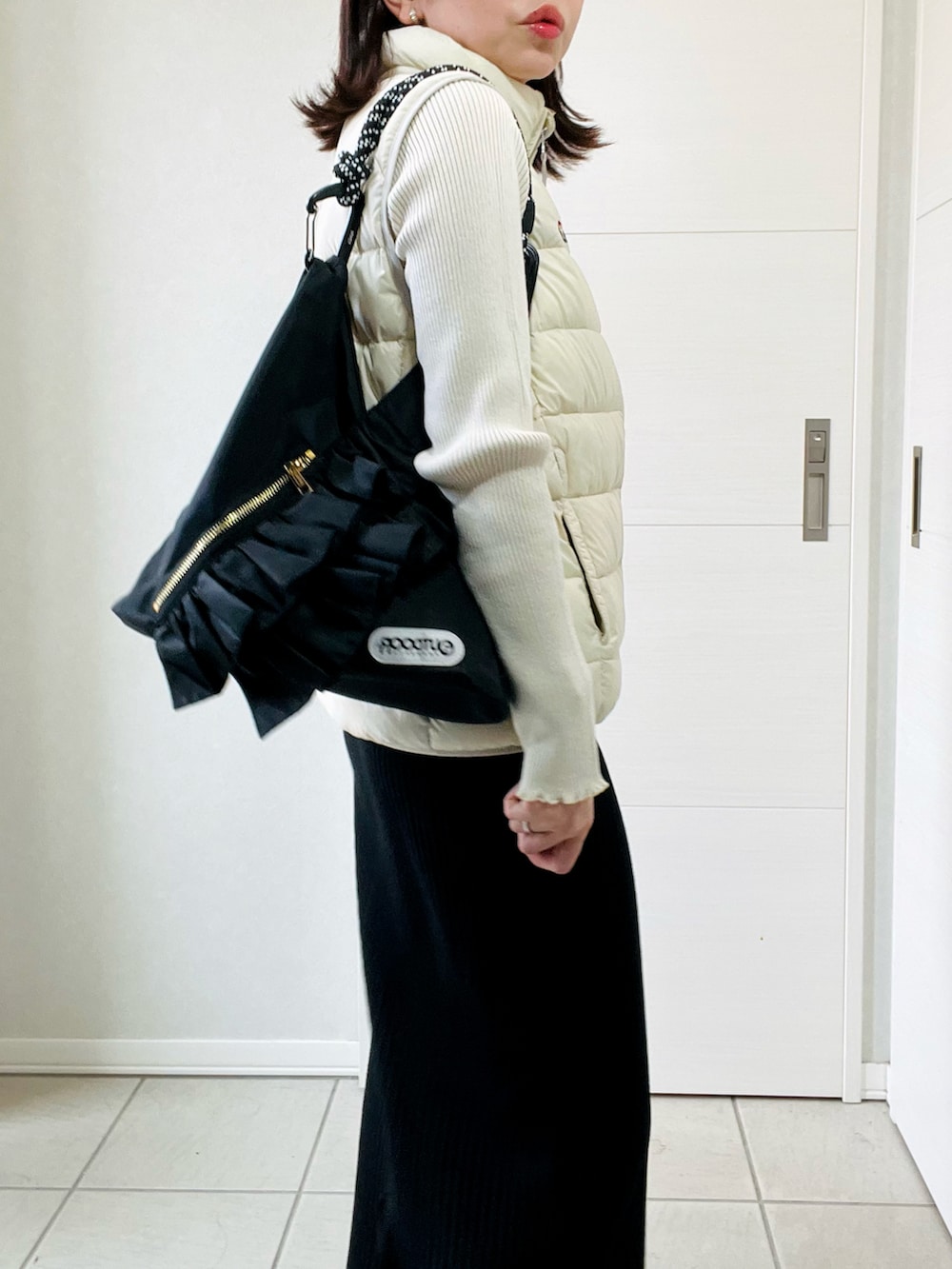 ホワイト系のダウンベスト、ホワイト系のニット/セーター、ブラック系のスカートを着用したレディースの秋コーディネートの3枚目の写真