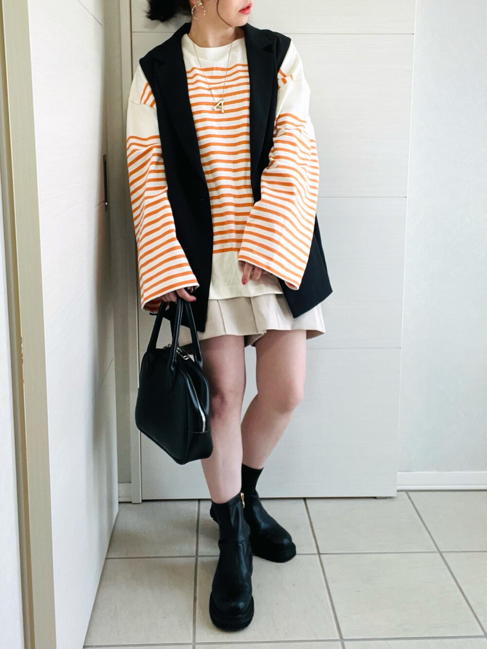 オレンジ系のTシャツ/カットソー、ブラック系のベスト、ホワイト系のスラックスを着用したレディースの春コーディネートの2枚目の写真