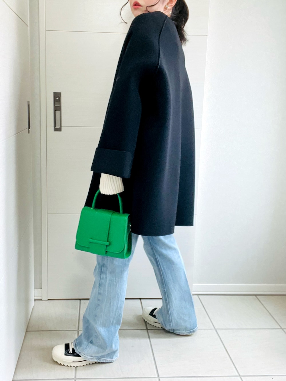 ブラック系のノーカラーコート、ホワイト系のTシャツ/カットソー、ブルー系のデニムパンツを着用したレディースの秋コーディネートの5枚目の写真