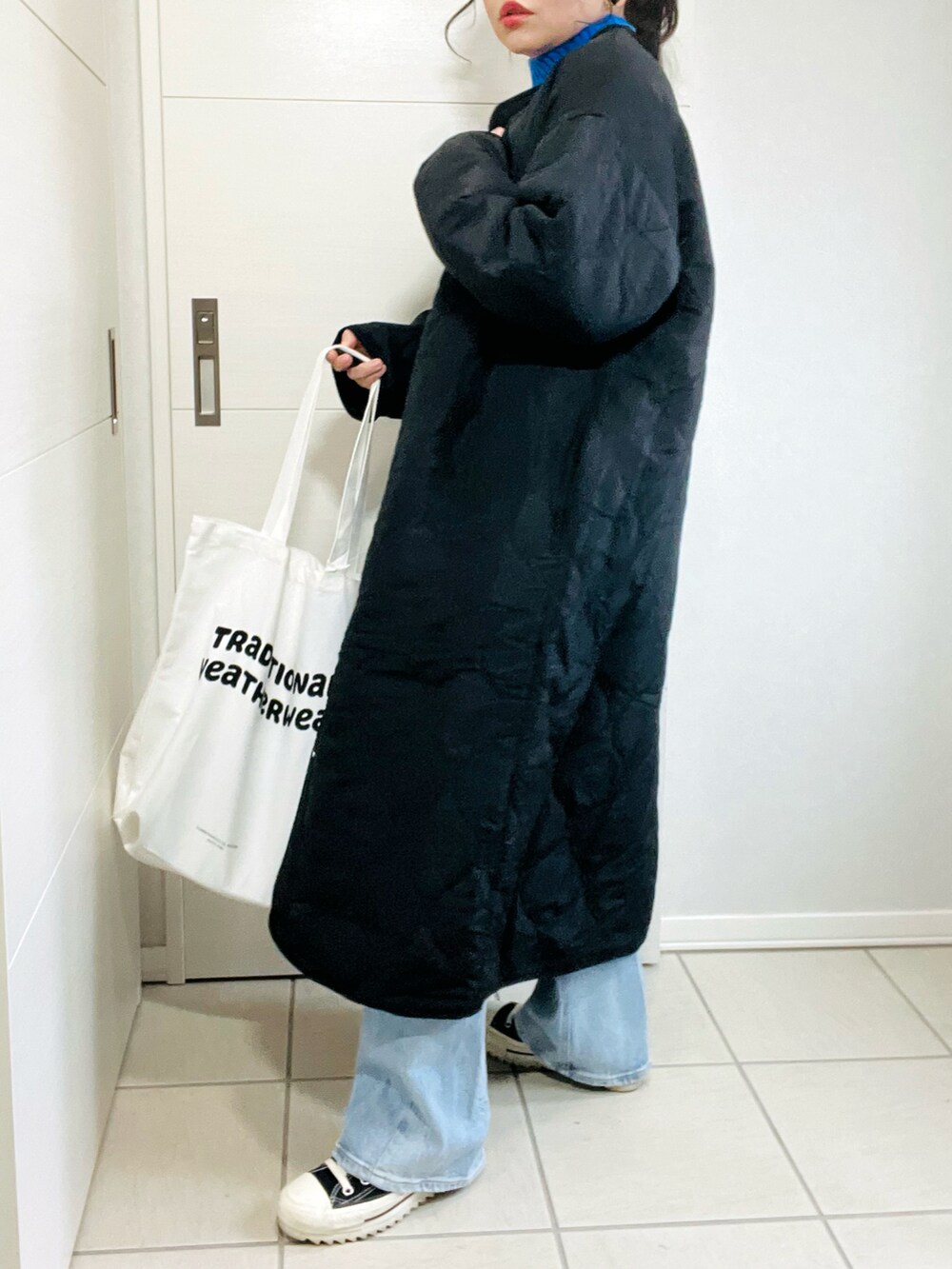 ブラック系のノーカラーコート、ブルー系のニット/セーター、ブルー系のデニムパンツを着用したレディースの秋コーディネートの4枚目の写真