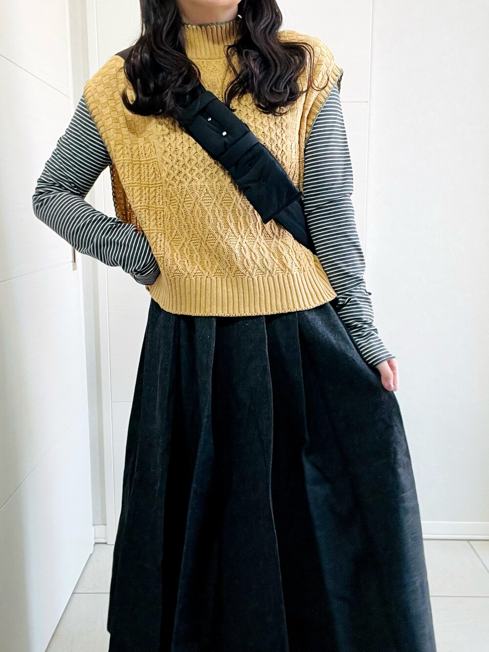 イエロー系のベスト、グレー系のTシャツ/カットソー、ブラック系のスカートを着用したレディースの秋コーディネートの4枚目の写真