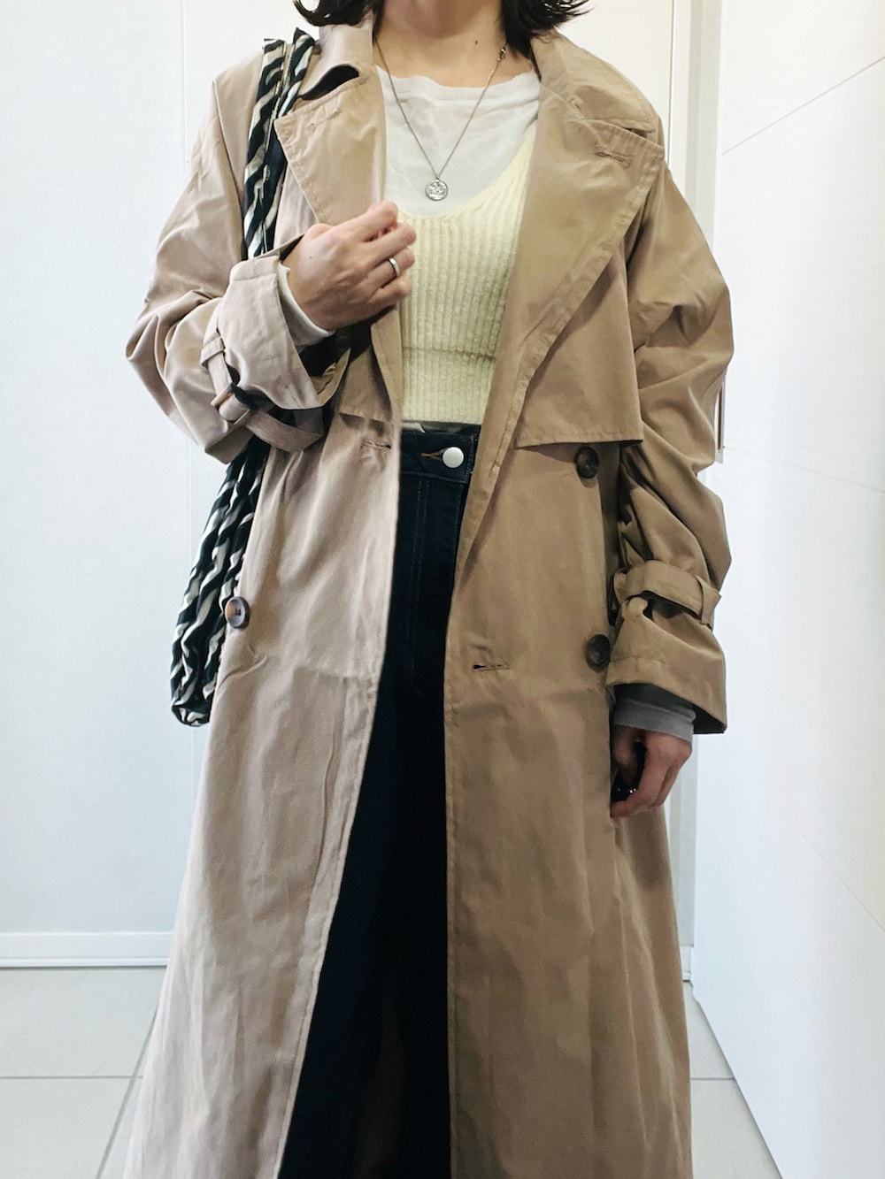 ベージュ系のトレンチコート、ホワイト系のニット/セーター、ブルー系のデニムパンツを着用したレディースの春コーディネートの2枚目の写真