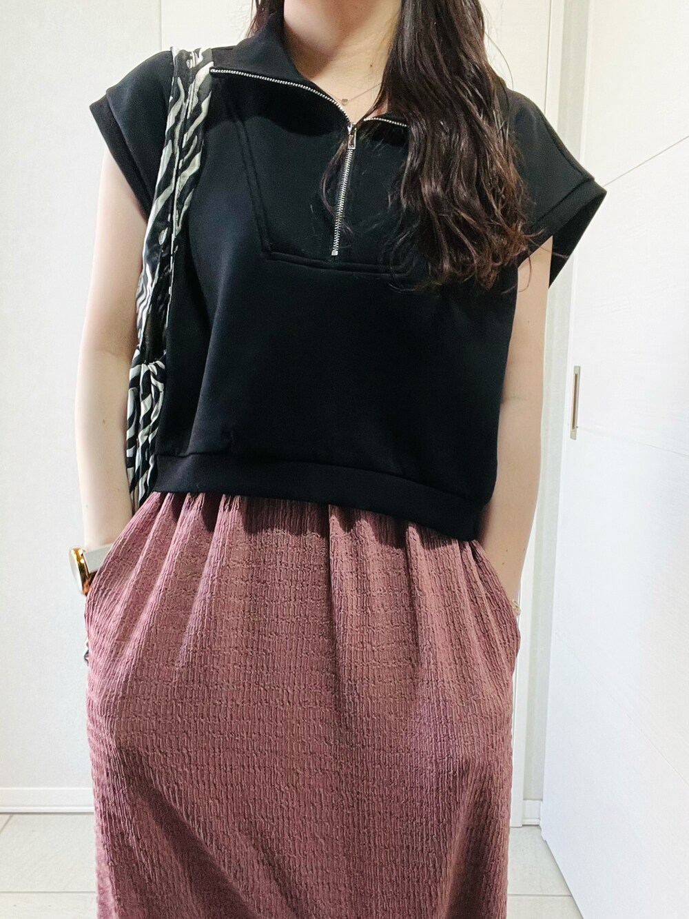 ブラック系のベスト、ピンク系のスカート、ブラック系のサンダルを着用したレディースの夏コーディネートの2枚目の写真