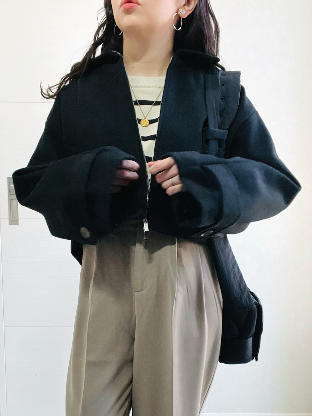 ブラック系のブルゾン、ホワイト系のニット/セーター、ベージュ系のスラックスを着用したレディースの秋コーディネートの3枚目の写真